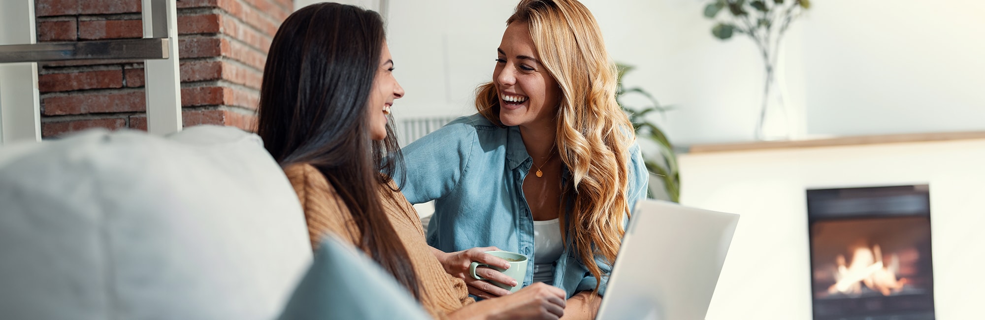 Dos mujeres sonrientes sentadas en un sofá delante de un ordenador portátil