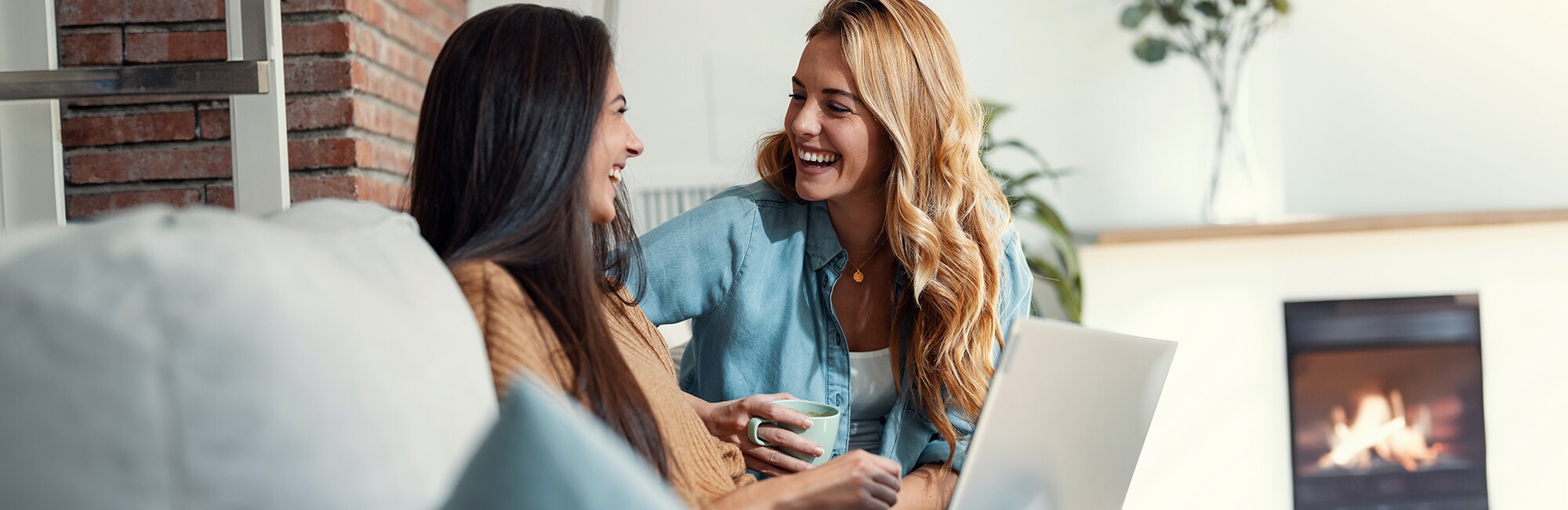 Dos mujeres sonrientes sentadas en un sofá delante de un ordenador portátil