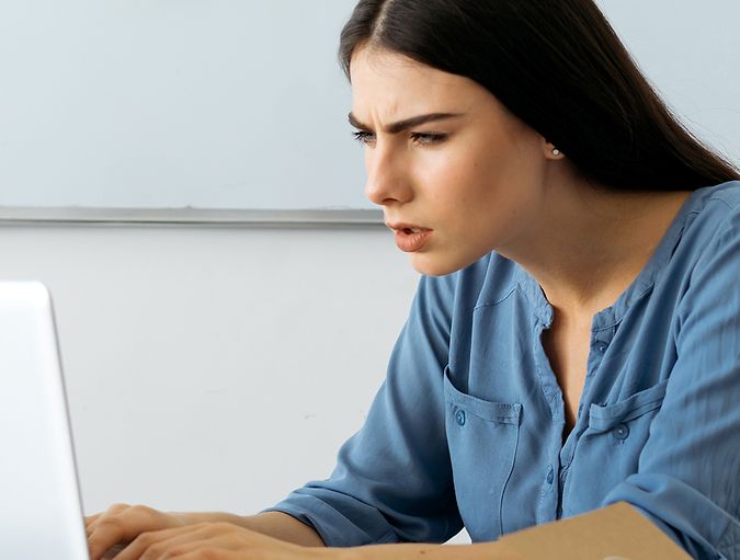 Mujer que frunce el ceño y entrecierra los ojos mientras mira su portátil